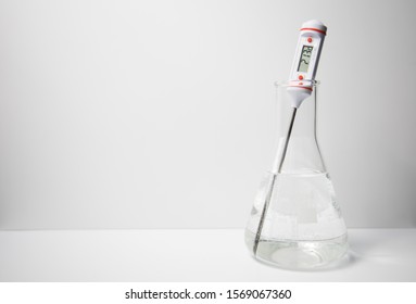 A digital thermometer measuring the temperature of a liquid in a glass erlenmeyer flask on a white background. Science experiment.