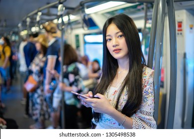 Digital Travel Concept. Young Asian Woman Traveling By The Train Or Mass Rapid Transit(MRT) Train Near The Window Using Smartphone In A Subway, She Texting Message And Watching Movie On Mobile Phone 