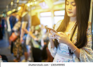 Digital Travel Concept. Young Asian Woman Traveling By The Train Or Mass Rapid Transit(MRT) Train Near The Window Using Smartphone In A Subway, She Texting Message And Watching Movie On Mobile Phone 