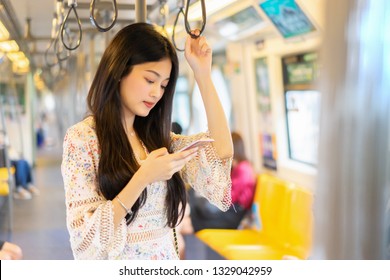 Digital Travel Concept. Young Asian Woman Traveling By The Train Or Mass Rapid Transit(MRT) Train Near The Window Using Smartphone In A Subway, She Texting Message And Watching Movie On Mobile Phone 