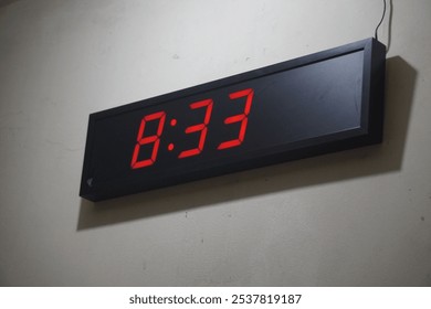 digital wall clock displaying the time "8:33" in red numbers on a black background. The clock is mounted on a light-colored wall with a visible wire connected to it - Powered by Shutterstock