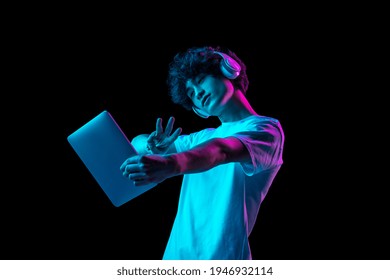 Digital world. Young man using tablet, device isolated over dark multicolored background in neon light. Future, gadgets, technology, education online concept. Human emotion, facial expressions. .