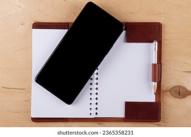 Digitalization concept. Paper notebook vs smartphone. Digital phone with blank black screen and empty  notebook lie on wooden table
