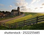 The dike alongside the sea shore (Wadden Sea) at sunset in the terp village Wierum, Friesland, Netherlands, with the reformed St Mary