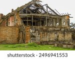 Dilapidated brick building with collapsed roof. Exposed wooden beams and circular windows. Crumbling walls and overgrown vegetation. Abandoned structure in tropical setting. Architectural ruins showin