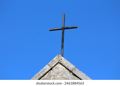 Dilapidated old worn down black metal cross on top of traditional Catholic stone church partially covered with yellow moss on clear blue sky background - Powered by Shutterstock