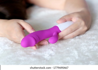 Dildo in female hands close up. Woman on a bed with purple silicone vibrator for sex games