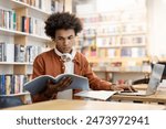 Diligent black guy deeply engrossed in reading book, sitting in brightly lit university library, preparing for lecture or tests