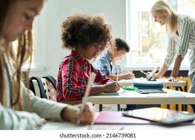 Diligent concentrated hard working diverse miltiethnic classmates schoolchildren writing tasks in notebooks with happy teacher explaining and helping. Schoolwork in diversity team. Education concept.