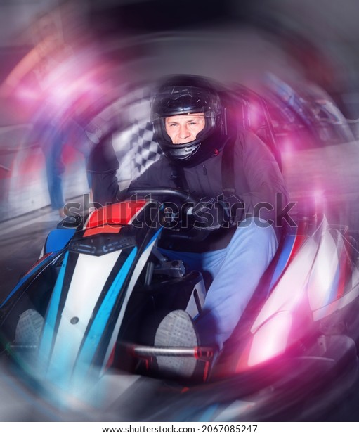 Diligent\
efficient man in helmet driving car for karting in sport club,\
friendly smiling woman with flag on\
background
