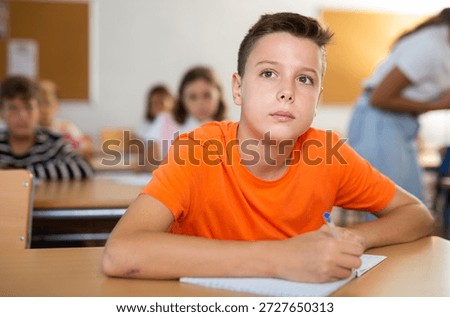 Diligent elementary school student tween boy studying with classmates, making notes of teacher lecture