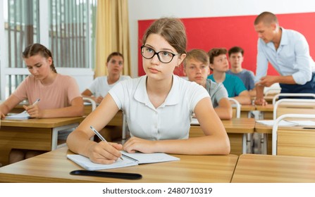 Diligent high school student teenage girl studying in college with classmates, making notes of teacher lecture - Powered by Shutterstock