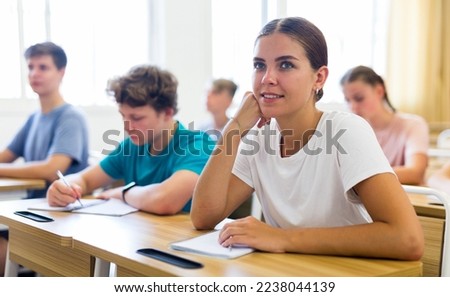 Diligent high school student teenage girl studying in college with classmates, making notes of teacher lecture