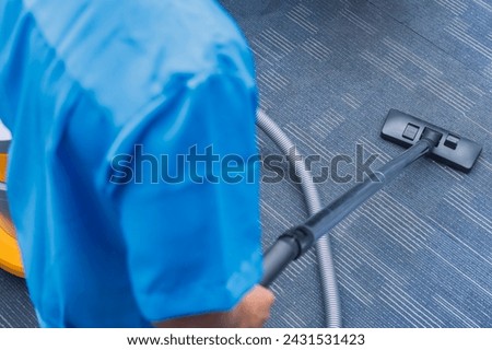 A diligent janitor thoroughly cleans the carpet with a vacuum cleaner. Anonymous behind the shoulder shot.