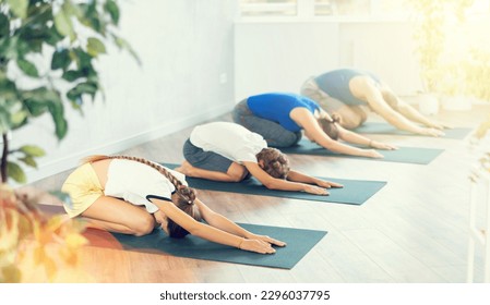 Diligent preteen girl practicing child's pose of yoga on black mat together with her parents - Powered by Shutterstock