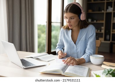Diligent student woman studying sit at desk with laptop and textbook, makes notes, writing essay looks concentrated. Self-education, e-learning, university exams or admission preparation, tech concept - Shutterstock ID 2179531111