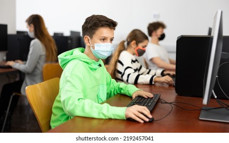 Diligent Tween Boy In Protective Face Mask Studying With Classmates In Modern Computer Lab At School During Coronavirus Pandemic. Concept Of Compelled Precautions