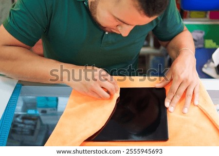 A diligent young man applying a screen protector to a tablet in a cell phone shop