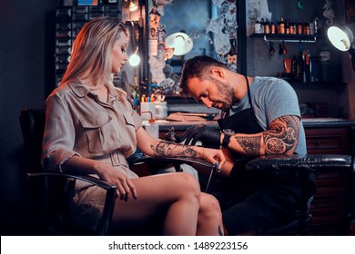 Dilligent Focused Tattoo Artist Is Creating New Tattoo On Young Woman's Hand At Tatoo Studio.