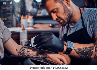 Dilligent Focused Tattoo Artist Is Creating New Tattoo On Young Woman's Hand At Tatoo Studio.