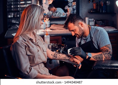 Dilligent Focused Tattoo Artist Is Creating New Tattoo On Young Woman's Hand At Tatoo Studio.