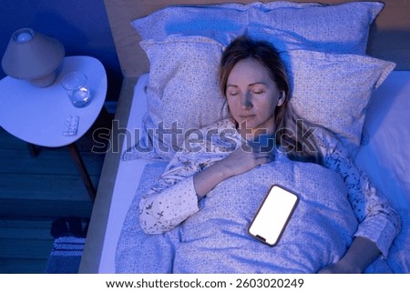 In a dim room lit only by the white glow of her phone, a woman fell asleep peacefully, placing her gadget next to her. The light from the screen illuminates the room. White phone screen