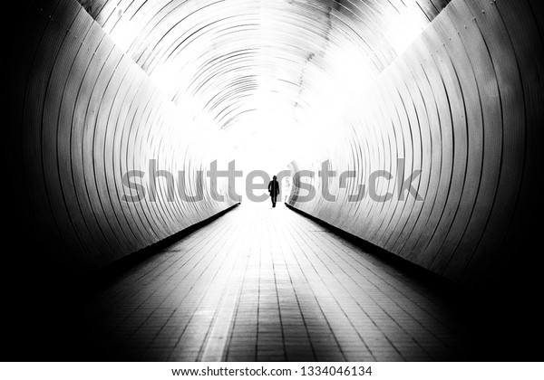 Diminishing perspective of unrecognizable man in\
a bright public tunnel in Stockholm, Sweden. The tunnel is a\
walking path between two\
streets.