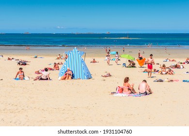 Dinard, Brittany, France - August 31, 2016: People sunbathe on fine sand by blue and white striped beach tents on Plage de l'Écluse, the main beach of this prestigious French seaside resort. 