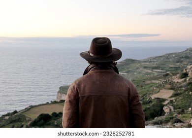 Dingli, Malta, 01-03-2012: Cliffs along the seashore near the village of Dingli, man in a wide-brimmed hat looks at the horizon, unrecognizable from behind