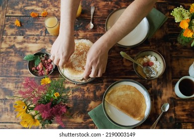 Dining Al Fresco Or Healthy Breakfast Outside. Man Eating Crepes Rolls With Curd. Food On Wooden Table Overhead View.