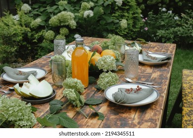 Dining in backyard garden. Summer table set for brunch. Wooden table decorated fresh flowers and fruits. Dining al fresco.