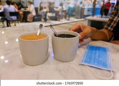 Dining Concept During Covid-19 Phase 2: Tea And Coffee On White Marble Dining Table In Cafe Restaurant; Face Mask On Table. Masks Could Be Removed When Eating At Food Centres; Reopening