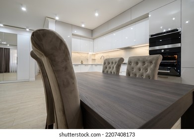 Dining room table and chairs, white spacious kitchen interior with television on the wall in the background and an oven with door open - Shutterstock ID 2207408173