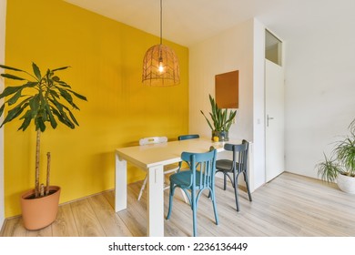 a dining room with yellow walls and wooden flooring, two blue chairs and a white table in the corner