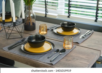 Dining Table With Black And Yellow Plate Setting In Modern Home.