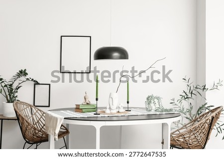 Dining table with burning candles, tree branch and books in light room