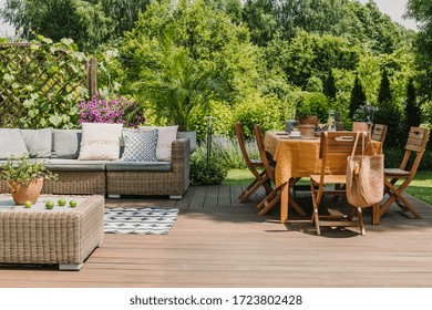 Dining table covered with orange tablecloth standing on wooden terrace in green garden