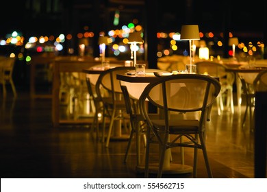 The Dining Table Illuminated By The City Lights. Night View Of A Restaurant.