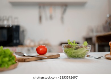 A dining table or kitchen table with a knife, a chopping board, and a bowl of fresh vegetables in a kitchen. Home cooking concept - Powered by Shutterstock