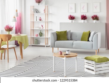 Dining Table With Olive Green Tablecloth In Bright Scandinavian Living Room With White And Wooden Furniture, Grey Sofa And Striped Carpet , Real Photo