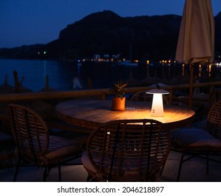 Dining Table On The Embankment At Night, Romantic Dining In Luxury Resort. Cafe On Beach With Seaview. Romantic Soft Warm Light Lamp On Table. Outdoor Cafe