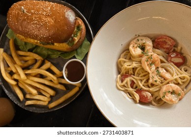 A dining table scene featuring two popular dishes: on the left, a gourmet burger with a sesame seed bun, green pesto, and lettuce, served with golden french fries and a dark dipping sauce in a bowl. On the right, a plate of spaghetti pasta with succulent shrimp, cherry tomatoes, and a creamy white sauce, garnished with fresh herbs. Both meals are presented in a rustic, appetizing style on dark wooden surfaces, highlighted by natural light.
