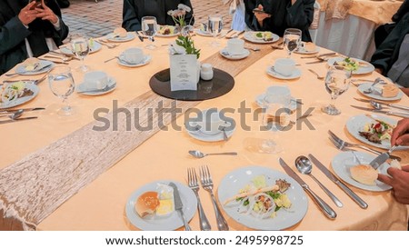 a dining table that has been prepared for a formal event. This dining table has a round shape and is covered with an elegant light orange tablecloth. In the middle of the table there is a centerpiece 