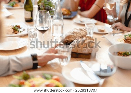 A dining table with wine glasses, bread, and various dishes. People enjoying a meal, sharing food, and socializing. Lunch and dining with friends. People at a fancy business lunch at restaurant.