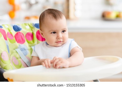 Dining Time. Adorable Baby Sitting In High Chair In Kitchen , Empty Space