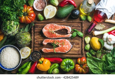 Dinner cooking ingredients. Raw uncooked salmon fish with vegetables, rice, herbs, spices and wine on chopping board over rustic wooden background, top view - Shutterstock ID 428425489