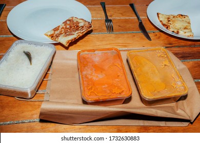 Dinner Delivered From Indian Restaurant. Take Away. Plastic Containers With Delicious Food On Table And Plates With Bread.