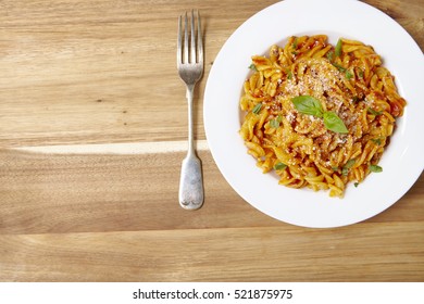 A Dinner Dish Full Of Tomato And Basil Fusilli Pasta On A Wooden Kitchen Counter Background With Fork And Empty Space At Side