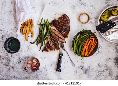 Dinner Food Tabletop. Overhead Of Bbq Fillet Steak Sliced With Potatoes, Carrot, Green Beans Fries On A Grey Table. Top View. 