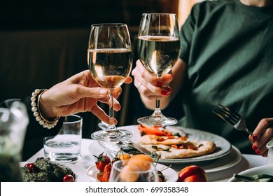 Dinner with friends of family served in a restaurant. Two glasses of white wine in hands